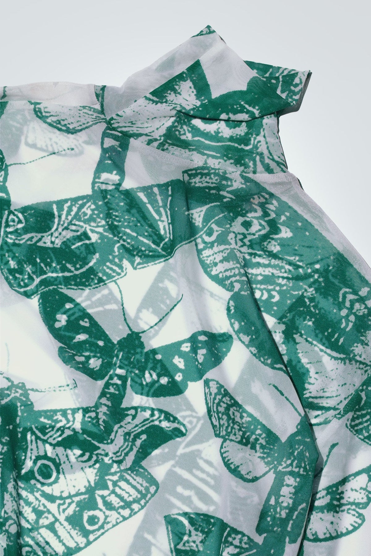 Green and white butterfly patterned top on a white background