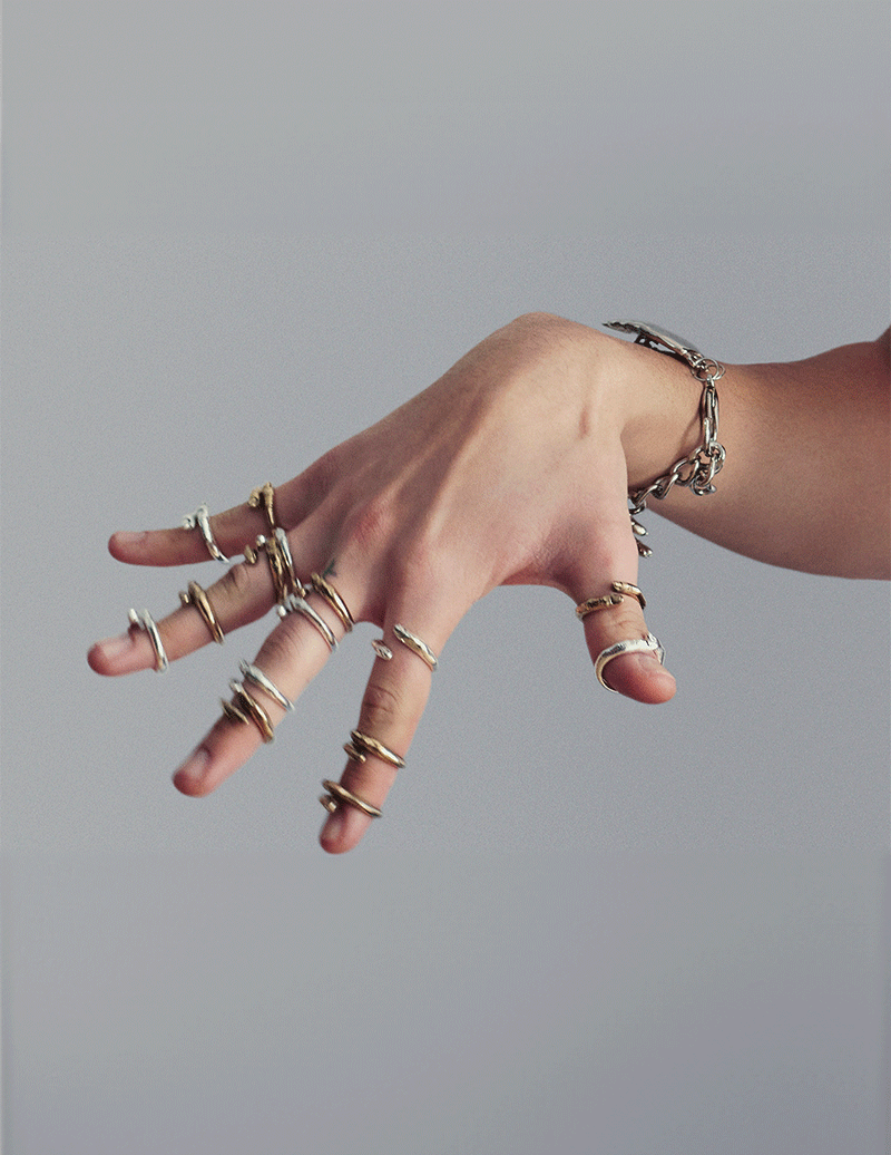 Hand wearing multiple gold and silver rings on a plain background