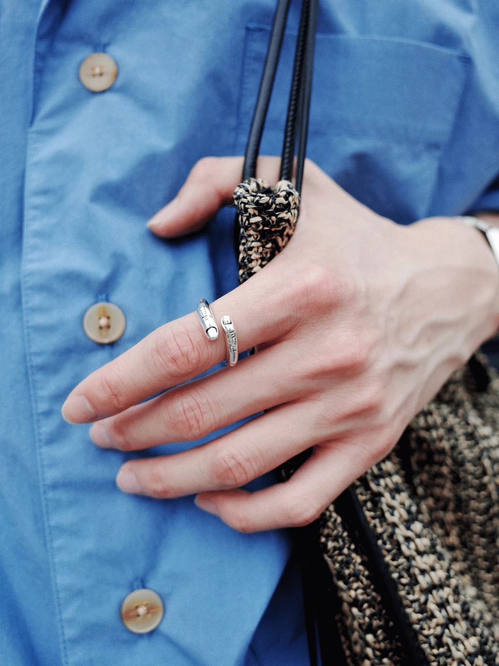 Close-up of a hand wearing a silver ring with a blue shirt in the background