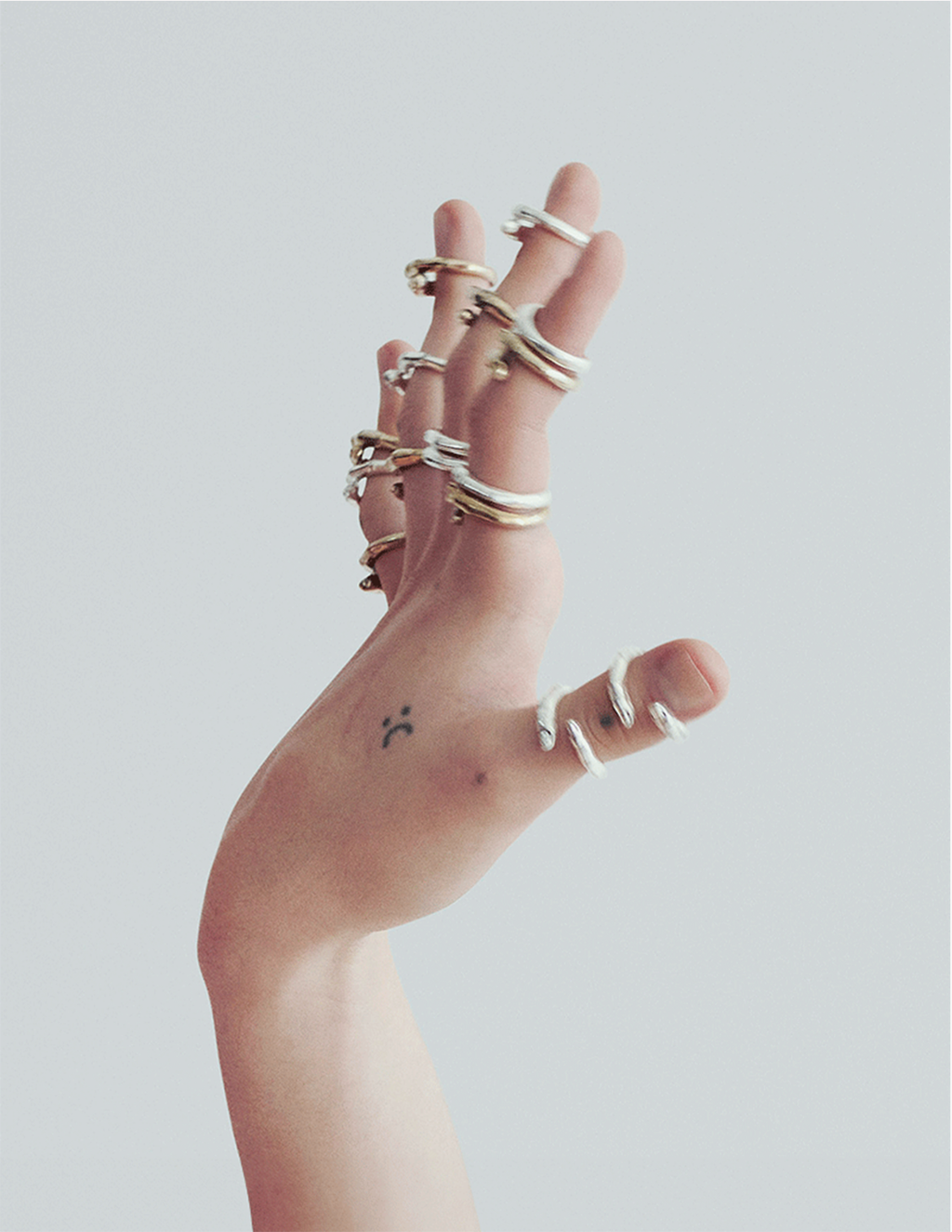 Hand with multiple silver and gold rings on a plain background