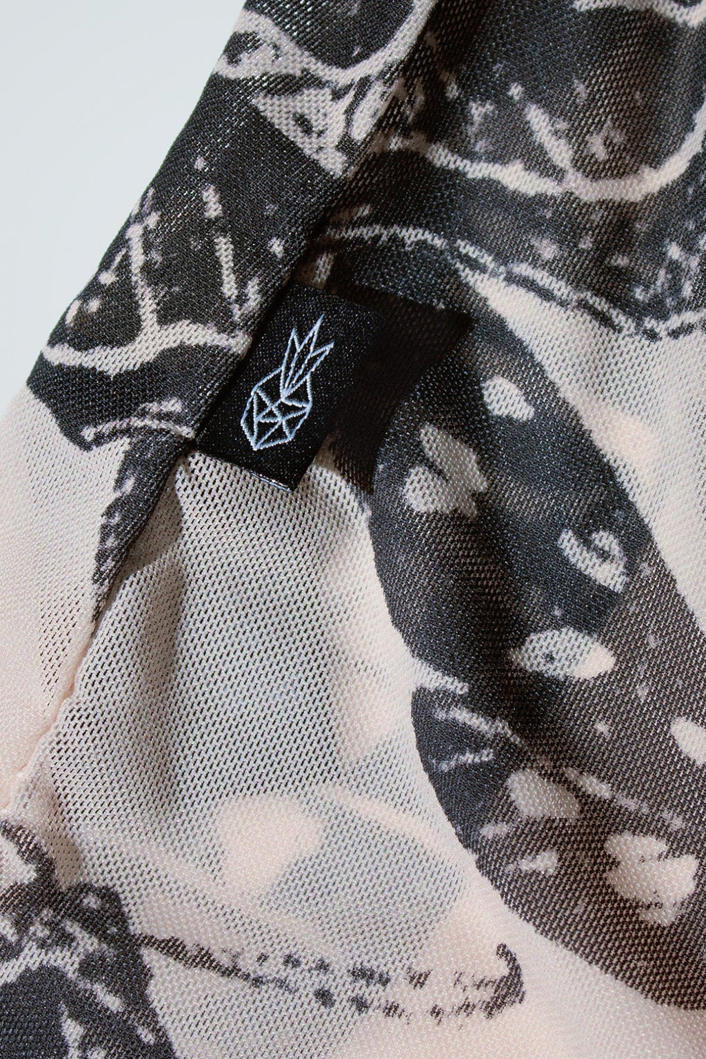 Close-up of black and nude patterned fabric with a logo on a white background