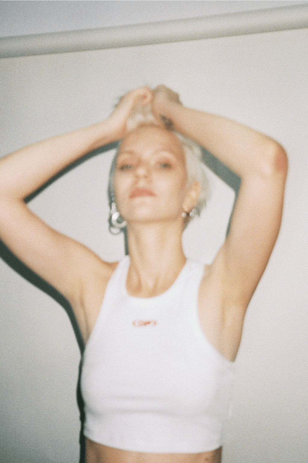 Person wearing a white tank top with a logo, standing against a plain background