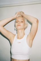 Person wearing a white tank top with a logo, standing against a plain background