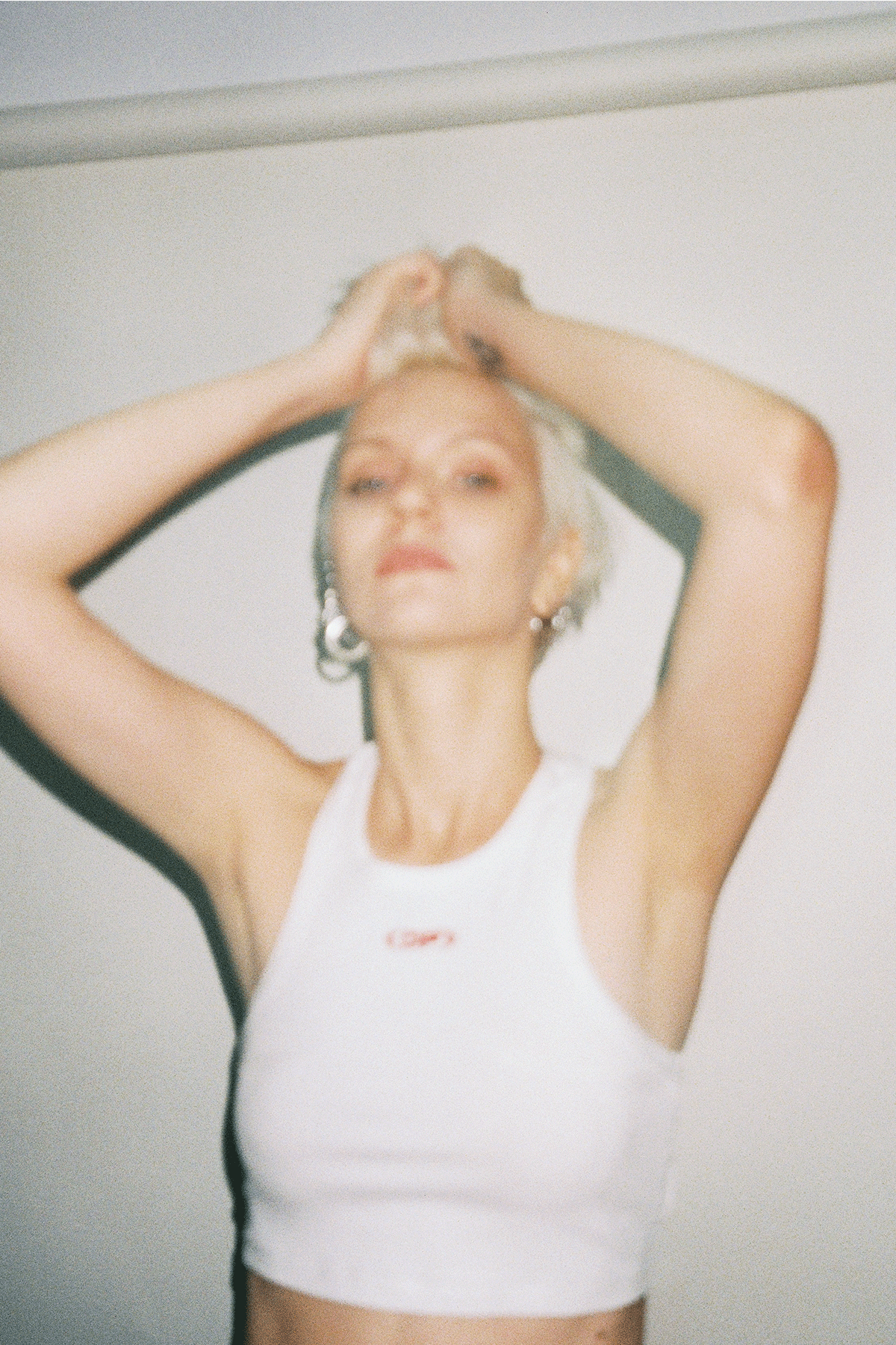Person wearing a white tank top with a logo, standing against a plain background