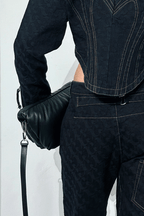 Person wearing a dark denim outfit with a black leather bag on a white background
