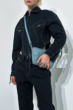 Person wearing a dark denim outfit holding a blue handbag against a white background